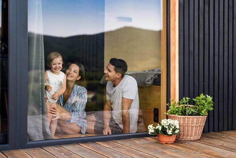 A young family with a small daughter looks out the window in their new home in the Pacific Northwest, financed with a credit union ARM loan.