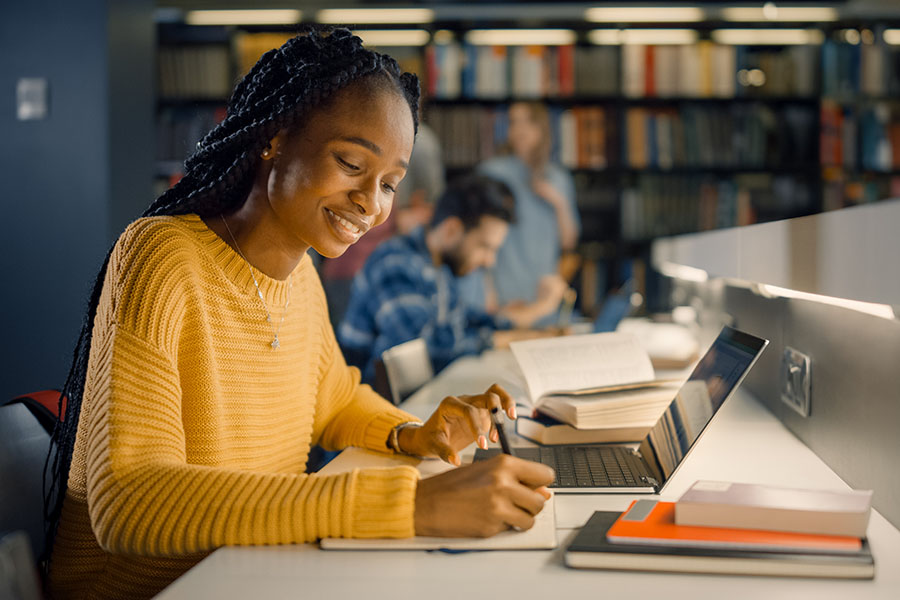 A young woman studying in the library smiles after getting approved for her student loan.