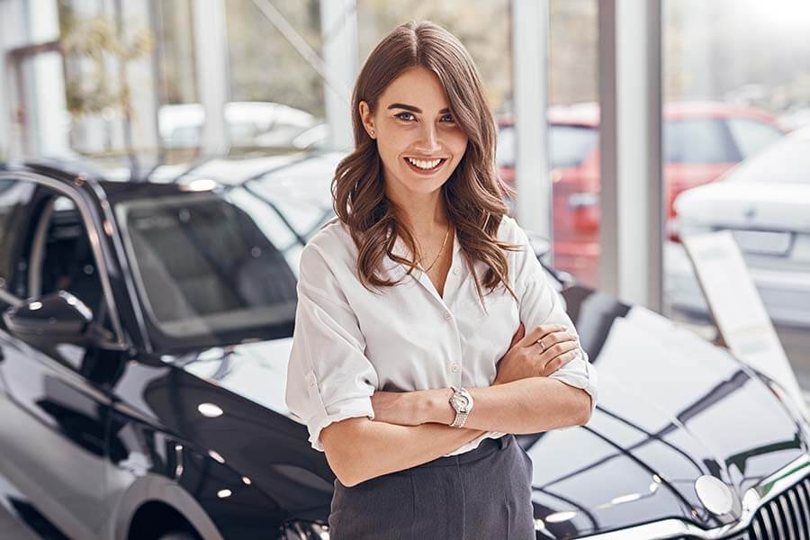 A woman smiling in front of her new car after financing it with a credit union auto loan.